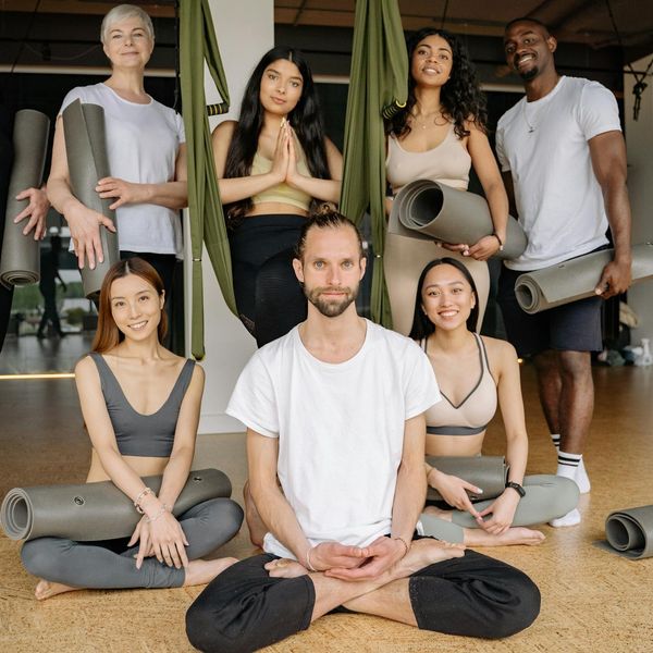 Diverse group of people smiling and sitting on yoga mats in a bright studio.