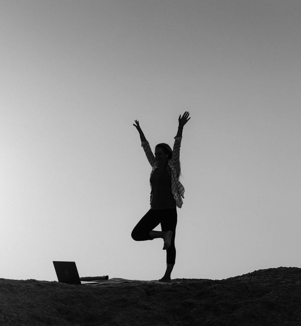 Silhouette of a person in a powerful yoga warrior pose against a sunrise.